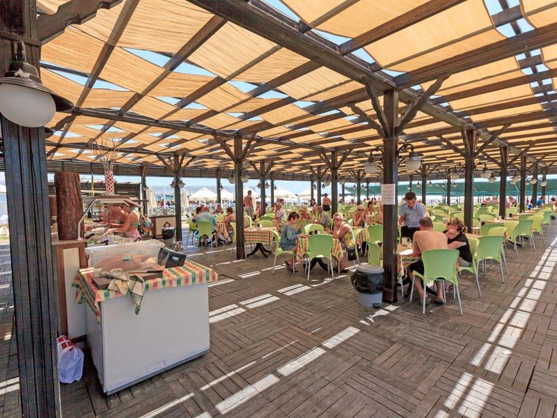 Terrazza coperta con ospiti seduti su sedie verdi sotto una tenda da sole.