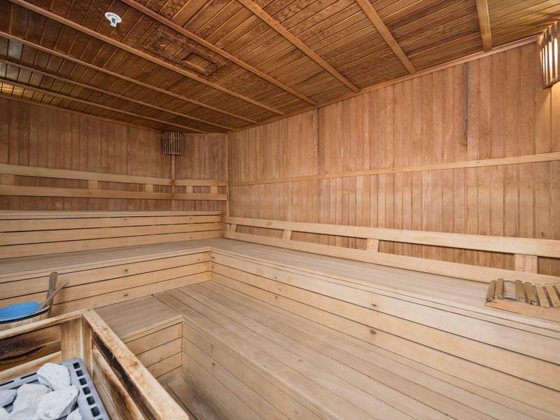 Interno di una sauna in legno chiaro con panche a più livelli e una stufa per sauna.