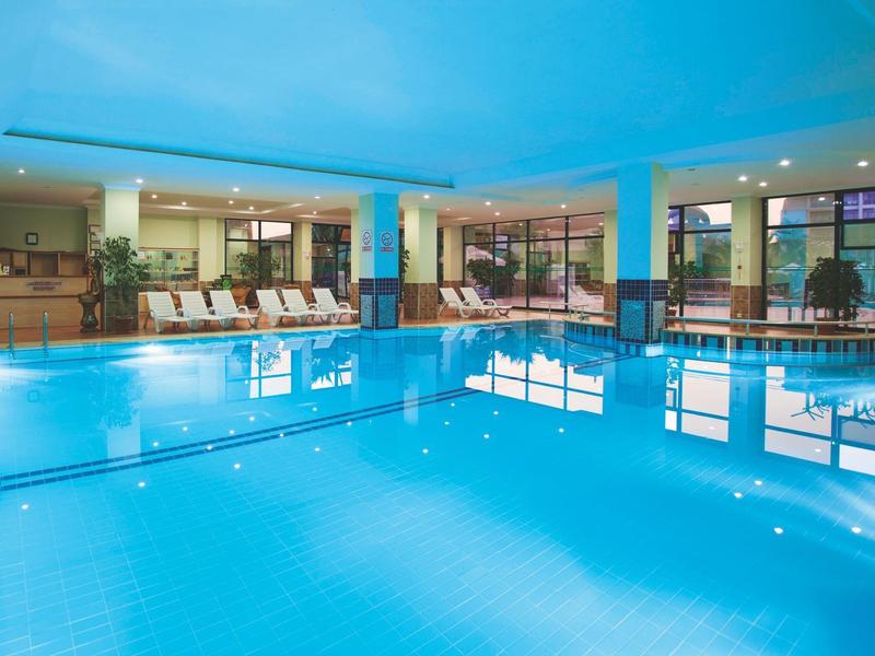 Piscina coperta con sedie a sdraio e grandi finestre in un hotel.