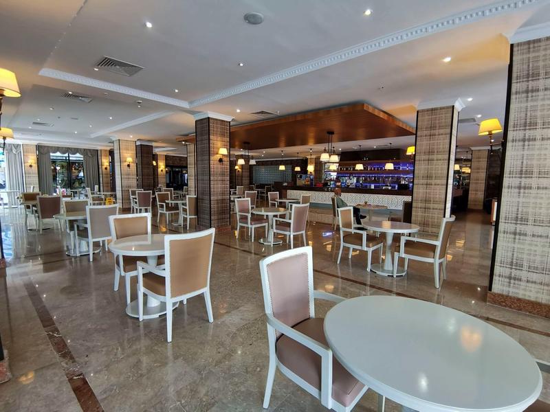 Area pranzo moderna con sedie e tavoli bianchi, pavimento in marmo chiaro e bar sullo sfondo.