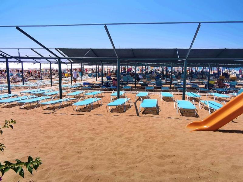 Spiaggia con ombrelloni, lettini e un'area giochi per bambini con scivolo sulla sabbia.