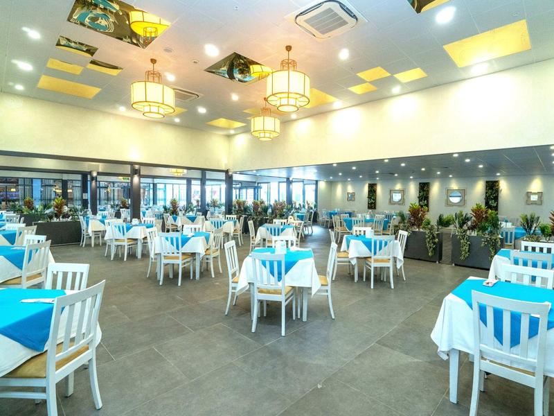 Ampia sala da pranzo luminosa con tavoli bianchi e tovaglie blu in un hotel.