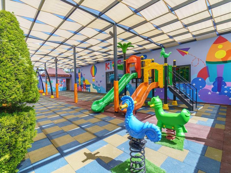 Colorato parco giochi per bambini con scivoli e cavalli a molla, coperto da un tetto trasparente.