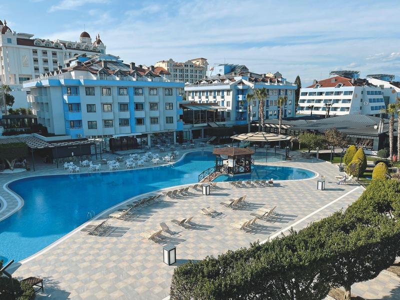 Grande piscina all'aperto con lettini davanti a hotel moderni sotto un cielo sereno.