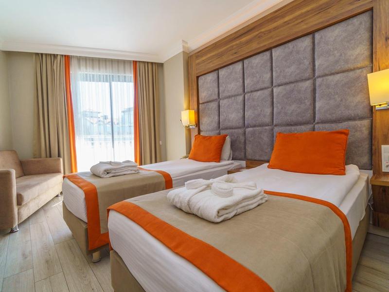 Camera d'hotel moderna con due letti singoli, accenti arancioni e finestra con luce naturale.