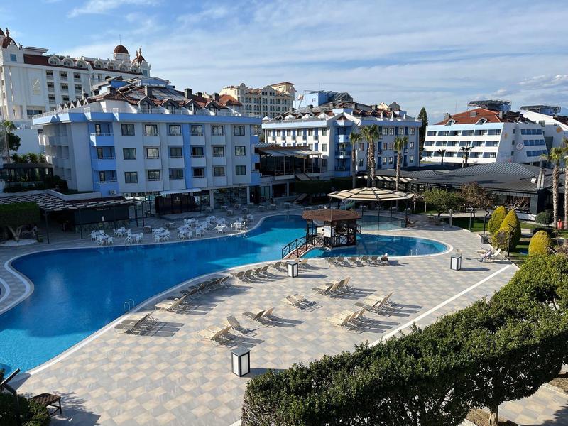 Hotel con grande piscina all'aperto circondata da lettini e edifici in stile mediterraneo sullo sfondo.