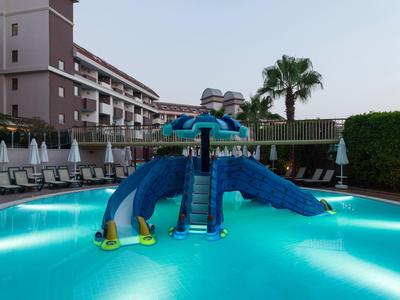 Kleines blaues Schwimmbad mit Wasserrutsche und umliegenden Liegestühlen bei Abendlicht.
