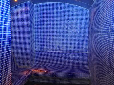 Enge blaue Mosaikwände und Sitzbank in einer gedämpft beleuchteten Dampfdusche.