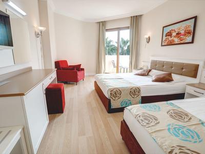 Helles Hotelzimmer mit zwei Betten, rotem Sessel, Balkon und moderner Einrichtung.
