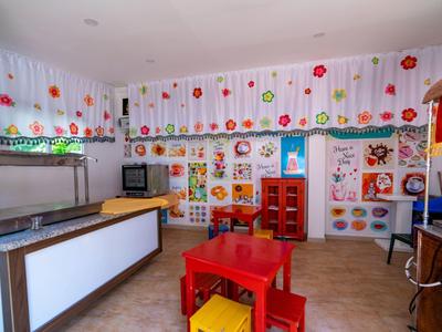 Hell eingerichteter Kinderraum mit bunten Malereien, rotem Tisch und Spielzeugregalen an der Wand.
