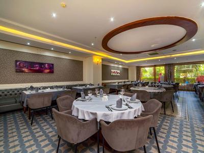 Elegantes Restaurant mit runden Tischen, braunen Stühlen und modernem Deckenlicht in warmen Farben.