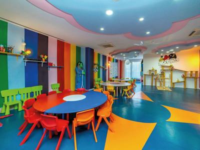 Bunter Kindergartenraum mit ovalem Tisch, kleinen Stühlen und fröhlicher Wandgestaltung.