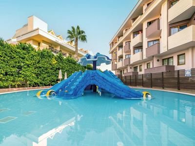 Kleines Schwimmbecken mit blauer Wasserrutsche neben mehrstöckigem Hotelgebäude und Palmen.