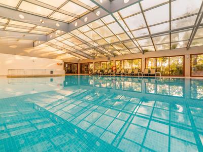 Hallenbad mit klarem blauem Wasser, gläsernem Dach und hellem, sonnendurchflutetem Raum.
