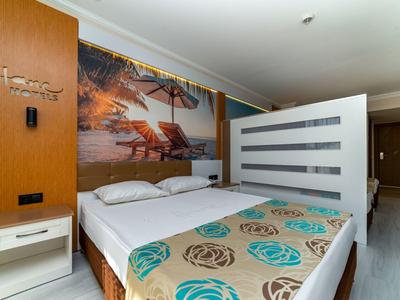 Helles Schlafzimmer mit großem Bett, buntem Bettüberwurf, Nachtisch und Wandbild mit Strandmotiv.