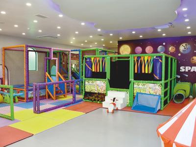 Kinder-Spielbereich mit bunten Klettergerüsten, weichen Matten und Weltraum-Dekoration an der Wand.