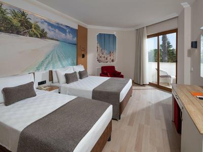 Modern hotel room with two double beds, balcony, and light wooden furniture.