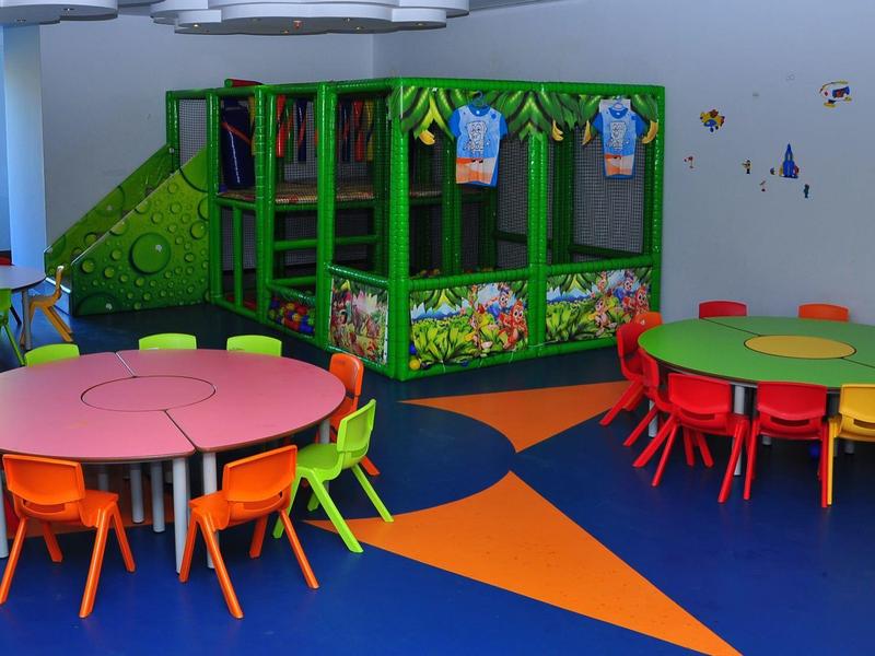 Colorful kids' playroom with tables, chairs, and a small climbing structure.