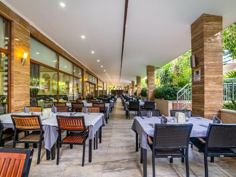 Covered outdoor hotel terrace with set tables and chairs under lighting.