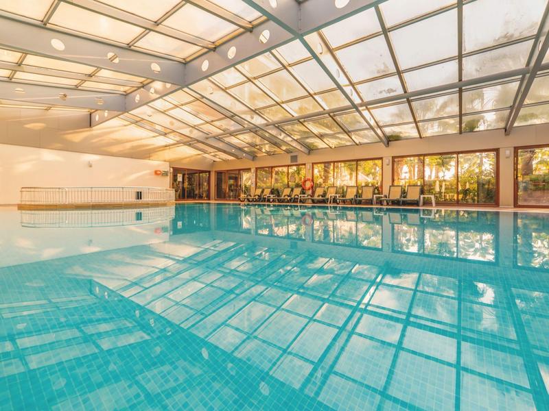 Bright indoor pool with glass roof and large windows reflecting the water.