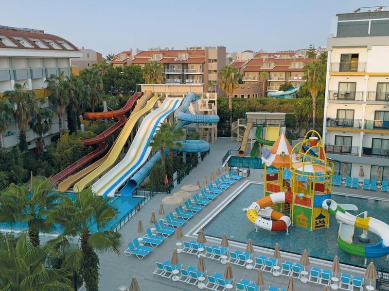 Hotel complex with multiple water slides, a children's pool, and sun loungers outdoors.