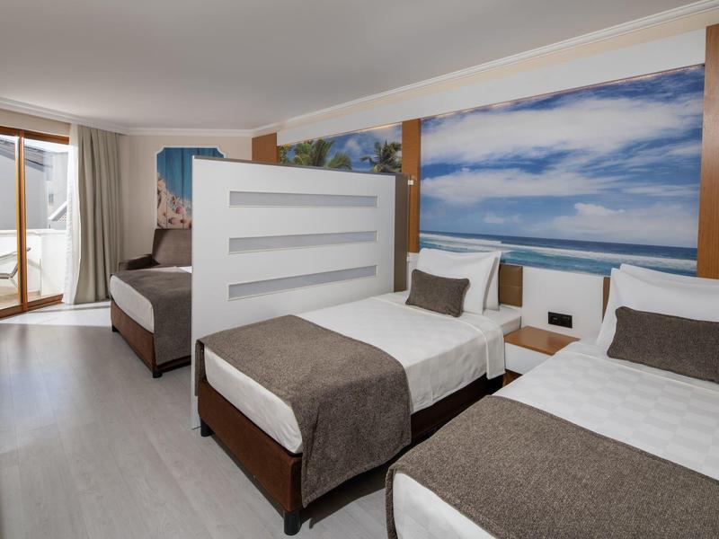 Hotel room with two single beds, wooden furniture, and access to a balcony overlooking the sea.