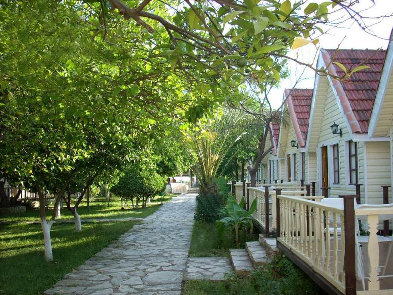 Pathway beside quaint cottages under lush green trees in a peaceful outdoor setting.