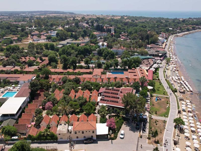 A coastal town with red-roofed buildings and a beach lined with umbrellas along the shoreline.