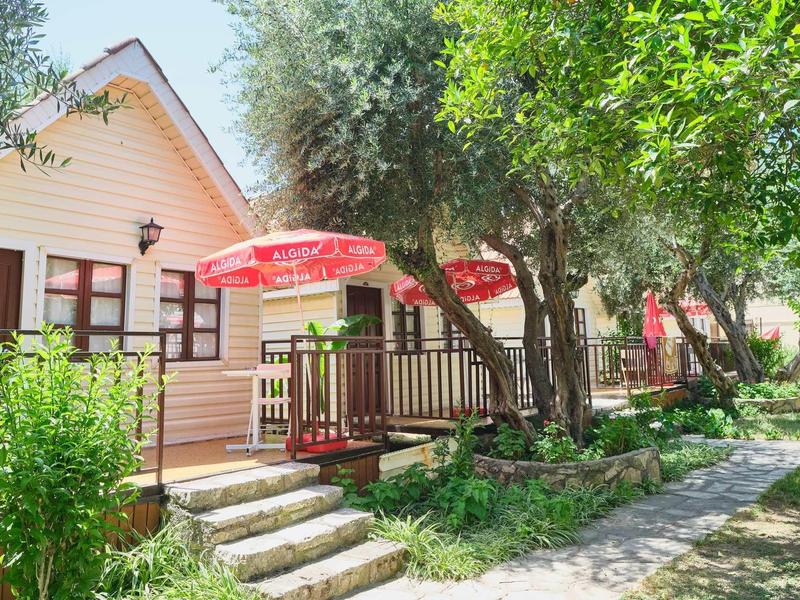 Cottages with red umbrellas and green trees along a stone pathway in a garden setting.