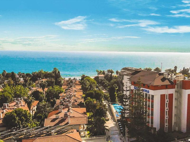 Vista su una città costiera con edifici residenziali, alberi e il mare sullo sfondo.