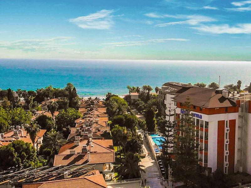 Vista di un resort con piscina circondato da alberi che si affaccia sul mare blu sotto un cielo sereno.