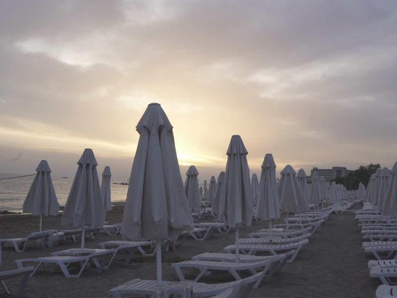 Lettini vuoti e ombrelloni chiusi sulla spiaggia al tramonto.