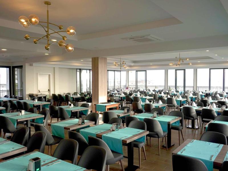 Ampia sala da pranzo luminosa con molti tavoli e sedie, ciascuno con tovaglie blu.