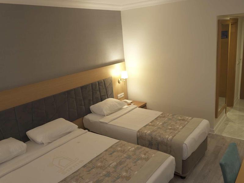 Camera d'albergo con due letti singoli, comodino e porta d'ingresso.