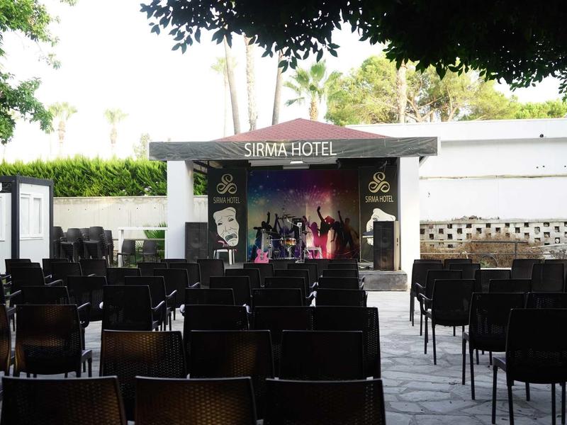 Palco all'aperto dell'hotel Sirma con file di sedie sotto gli alberi.