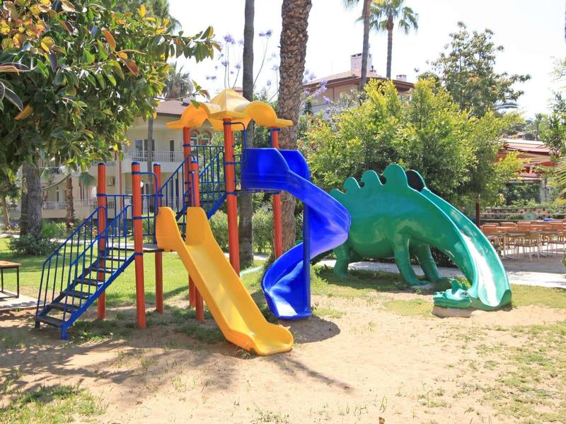 Area giochi per bambini colorata con scivoli in un giardino soleggiato con alberi.