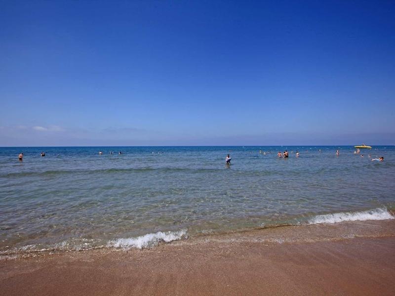 Mare blu limpido con pochi bagnanti e una spiaggia sabbiosa sotto un cielo sereno.
