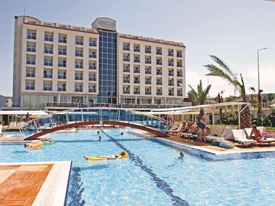 Grande hotel con piscina all'aperto, lettini e palme sotto un cielo sereno.