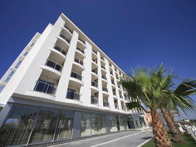 Edificio alberghiero bianco moderno con balconi sotto un cielo azzurro limpido e palme in primo piano.
