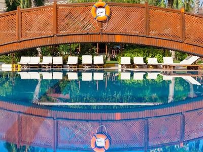 Ponte in legno sopra piscina turchese con lettini bianchi sullo sfondo