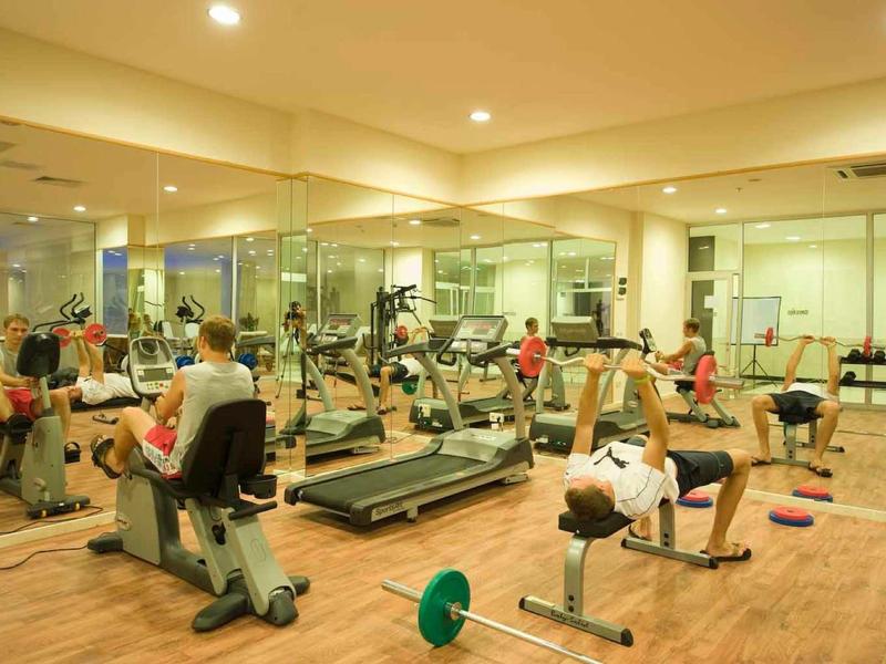 Palestra con più persone e varie attrezzature per esercizi, ben illuminata con grandi specchi.