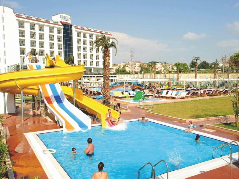 Hotel con piscina all'aperto e scivoli d'acqua, circondato da lettini e palme.