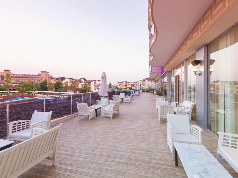 Ampia terrazza con sedie e tavoli bianchi accanto a un hotel con vista sulla città.