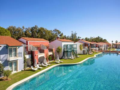 Modern villas with red roofs line a clear blue pool under a sunny sky.