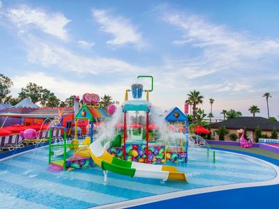 Colorful water playground with slides and fountains in a shallow pool under a partly cloudy sky.