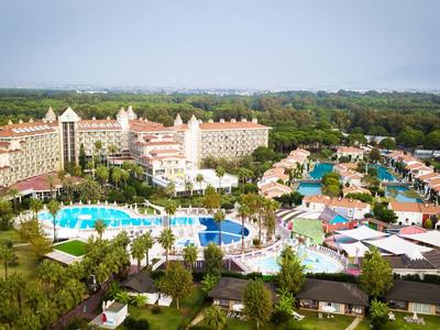 Large resort with multiple buildings, big pools, and abundant greenery under cloudy sky.