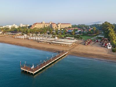 Blick auf einen Strand mit Steg, Sonnenschirmen und einem großen Resort im Hintergrund.