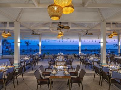Open-air restaurant with rows of tables and ocean view at dusk