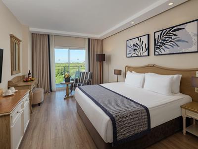 Modernes Hotelzimmer mit großem Doppelbett, Holzboden und Balkon mit grüner Aussicht.