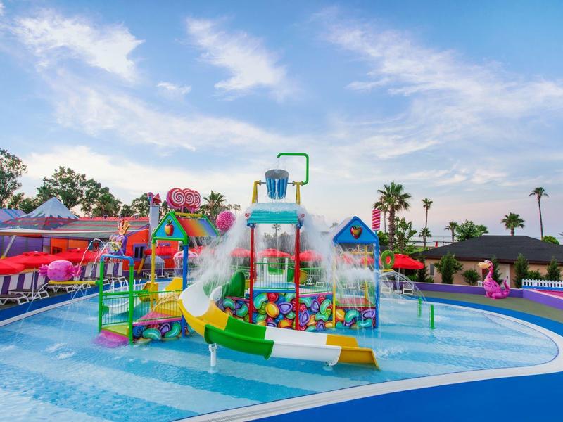 Colorful water playground with slides and fountains in a shallow pool under a partly cloudy sky.